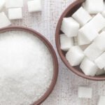 Une pile de morceaux de sucre blanc avec un verre de thé à la menthe marocain en arrière-plan, symbolisant la consommation de sucre au Maroc.