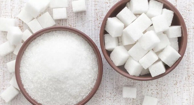 Une pile de morceaux de sucre blanc avec un verre de thé à la menthe marocain en arrière-plan, symbolisant la consommation de sucre au Maroc.