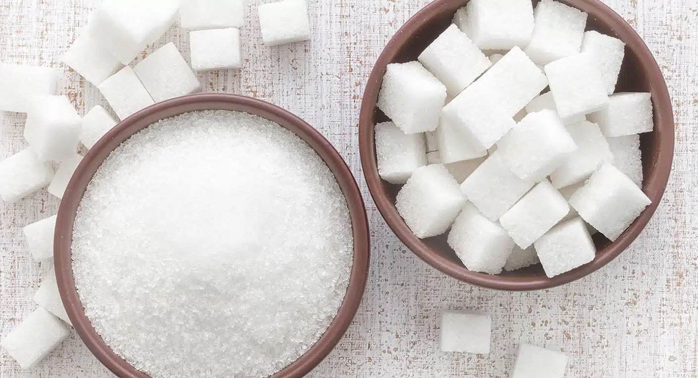 Une pile de morceaux de sucre blanc avec un verre de thé à la menthe marocain en arrière-plan, symbolisant la consommation de sucre au Maroc.