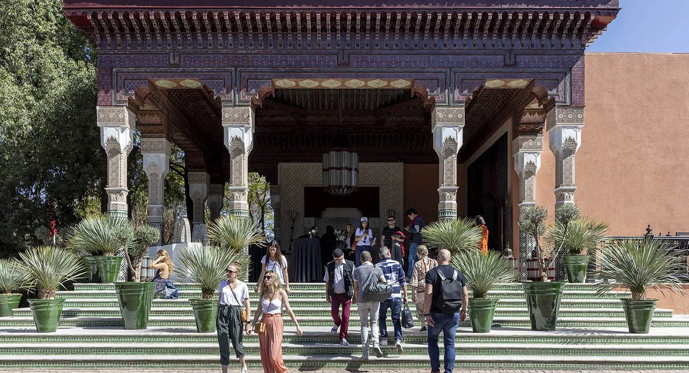 Vue panoramique de La Mamounia à Marrakech, avec des œuvres d'art contemporain africain exposées dans ses jardins luxuriants, sous un ciel bleu éclatant, symbolisant l'union de l'art et du patrimoine marocain.