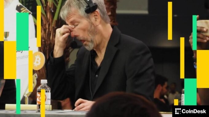 Michael Saylor speaking at a cryptocurrency conference with a Bitcoin logo in the background.