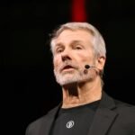 Michael Saylor's Risky Financial Gambit: The Unseen Pivot at MicroStrategy 4 Michael Saylor speaking, with Bitcoin and MicroStrategy logos in the background, symbolizing his financial strategy.