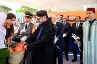 Sa Majesté le Roi Mohammed VI et SAR le Prince Héritier Moulay El Hassan lançant l'opération Ramadan 1447, entourés de paniers de denrées alimentaires et de bénévoles souriants.