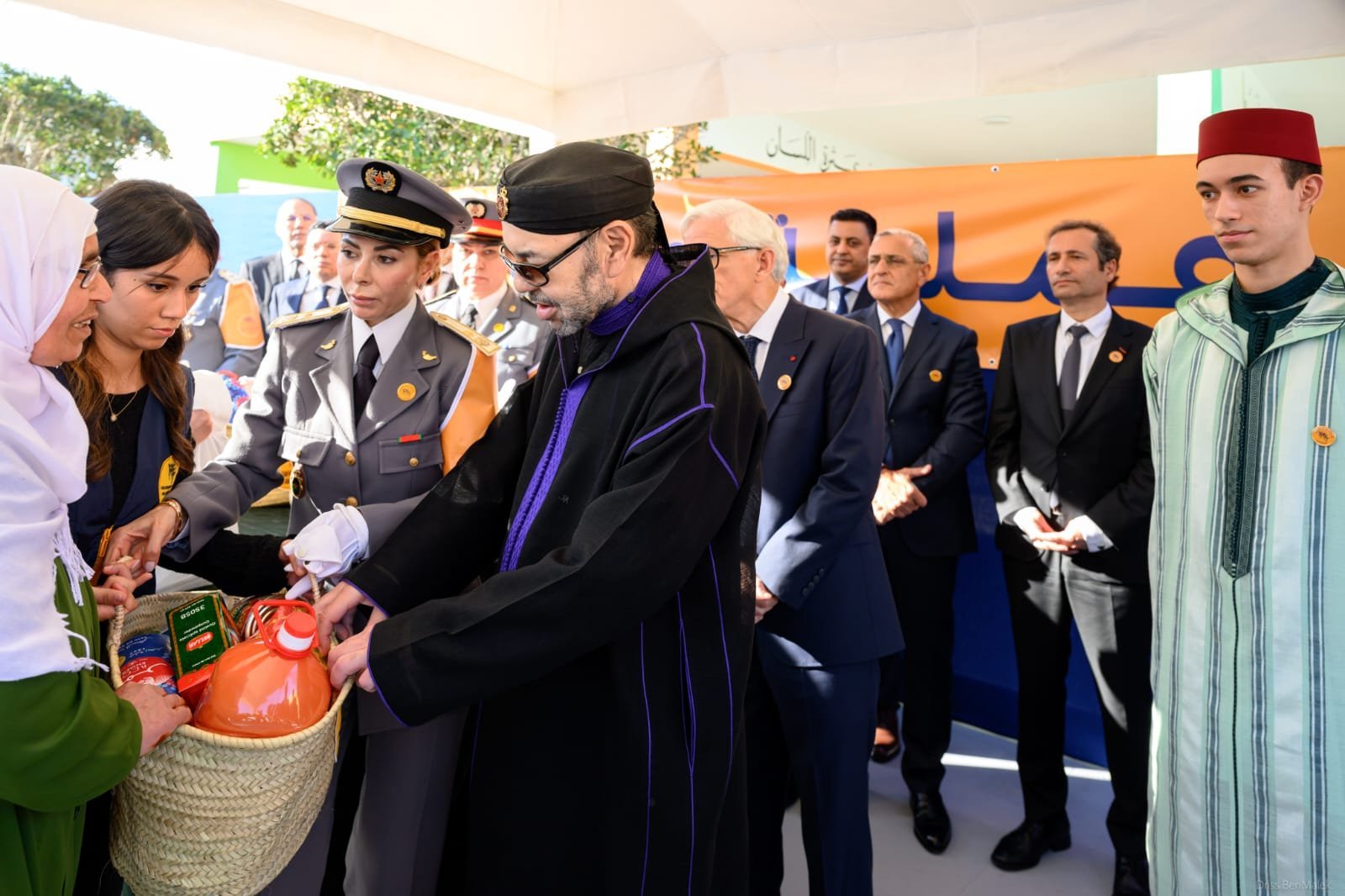 Sa Majesté le Roi Mohammed VI et SAR le Prince Héritier Moulay El Hassan lançant l'opération Ramadan 1447, entourés de paniers de denrées alimentaires et de bénévoles souriants.