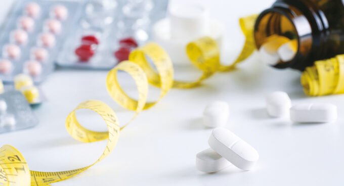 Une seringue d'injection amaigrissante posée à côté de pilules et d'un ruban à mesurer, symbolisant les différentes approches de la perte de poids.