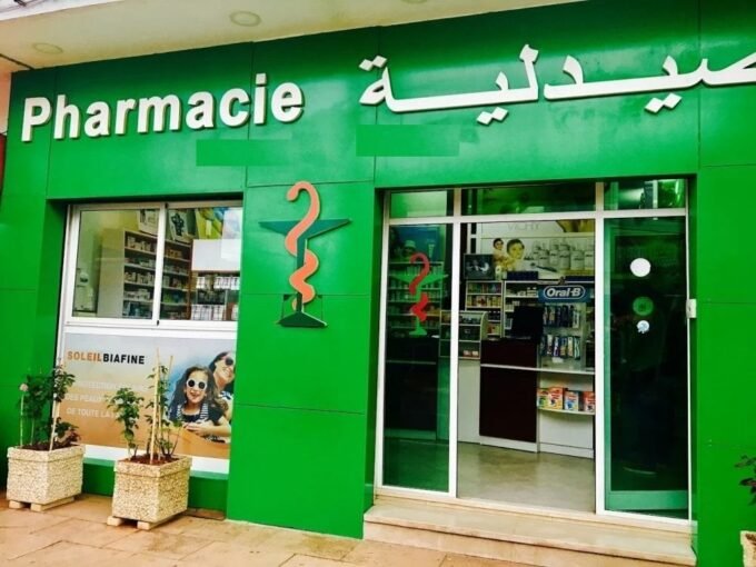 Un pharmacien marocain en blouse blanche, l'air déterminé, devant une rangée de médicaments, symbolisant la résistance de la profession face aux réformes proposées par le Conseil de la concurrence et la menace de grève.