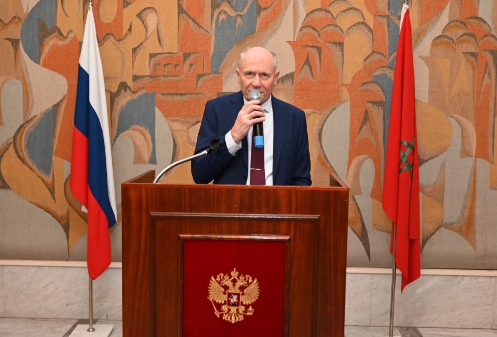 Le Maroc, Pilier de Stabilité et de Croissance : L'Ambassadeur Russe Salue une Coopération Fructueuse 3 L'ambassadeur de Russie au Maroc, Vladimir Baybakov, s'exprimant lors d'un événement diplomatique, avec un drapeau marocain et russe en arrière-plan.