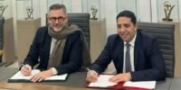 Deux dirigeants, Yves Peyrot Des Gachons de Stellantis Maroc et Hicham Kharrou d'Attawfiq Microfinance, se serrent la main devant un tricycle électrique FIAT TRIS, symbolisant leur partenariat pour la mobilité verte au Maroc.