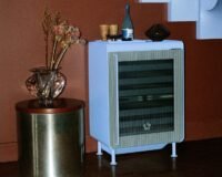 Rocco smart fridge in Ice Blue with fluted glass door, slender steel legs, and an accompanying tray, set in a modern living space.