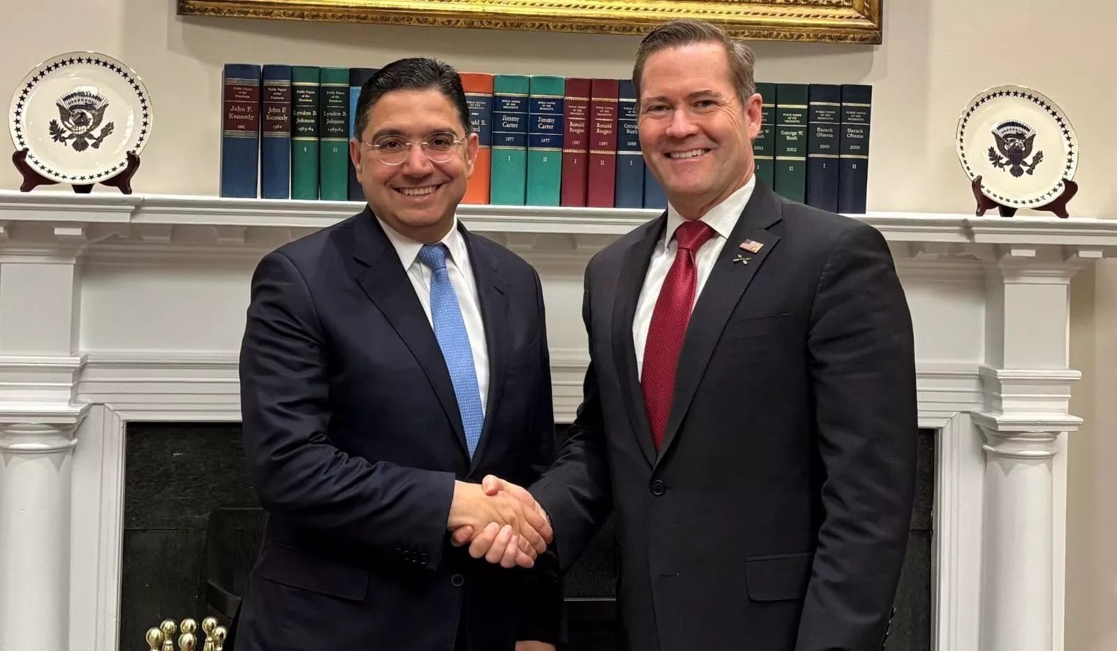 Représentation symbolique des drapeaux des États-Unis, de l'ONU, du Maroc, du Front Polisario, de l'Algérie et de la Mauritanie autour d'une table de négociation, illustrant les pourparlers à Madrid sur le Sahara.
