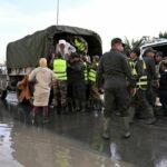 Vue aérienne de l'Oued Sebou en crue, avec des zones résidentielles proches des rives et des véhicules d'urgence en action pour l'évacuation des habitants à Sidi Kacem.