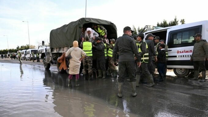 Vue aérienne de l'Oued Sebou en crue, avec des zones résidentielles proches des rives et des véhicules d'urgence en action pour l'évacuation des habitants à Sidi Kacem.