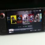 A Steam Deck handheld console displaying a game, with a backdrop suggesting a technological or futuristic theme.