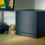 A sleek, black Valve Steam Machine console with a customizable LED light strip on the front, possibly next to a Steam Controller.