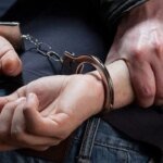 Un homme menotté, potentiellement un suspect de trafic de drogue, escorté par des policiers.