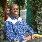 Portrait de l'écrivain guinéen Tierno Monénembo à Conakry, regardant au loin avec une expression pensive.