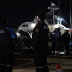 Illustration d'une embarcation de migrants en mer, avec des garde-côtes en arrière-plan, symbolisant une opération de sauvetage ou un drame maritime.