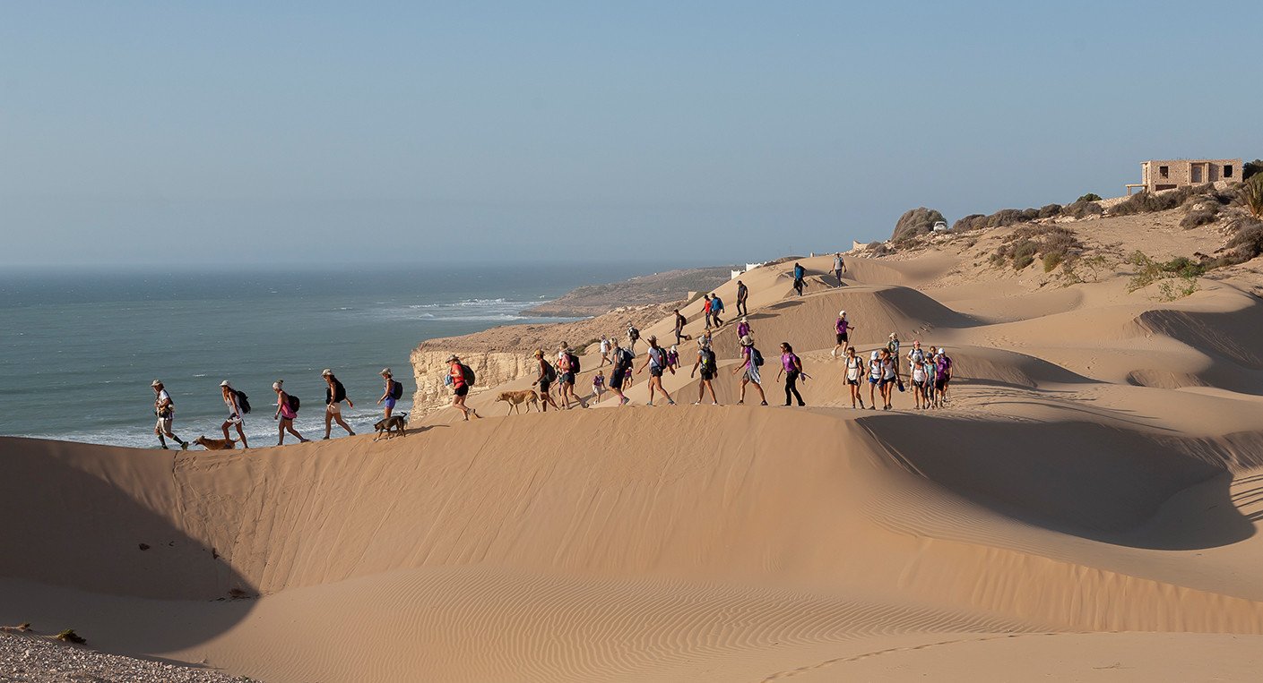 Groupe de femmes en pleine randonnée dans un paysage marocain ensoleillé, symbolisant l'aventure et la solidarité du Trek des Gazelles.