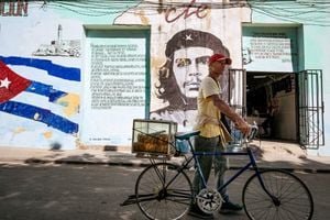A man sells pastries in Havana, Cuba, in front of a mural of Che Guevara, symbolizing the enduring Cuban Revolution amidst new political pressures.