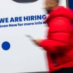 A 'now hiring' sign displayed in a Manhattan business window, symbolizing the state of the job market.