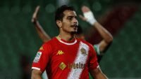 Wissam Ben Yedder, ex-attaquant de l'équipe de France et joueur du Wydad, souriant sur un terrain de football, symbolisant le soulagement après l'annulation de son procès.