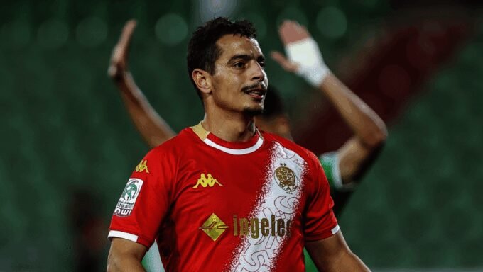 Wissam Ben Yedder, ex-attaquant de l'équipe de France et joueur du Wydad, souriant sur un terrain de football, symbolisant le soulagement après l'annulation de son procès.