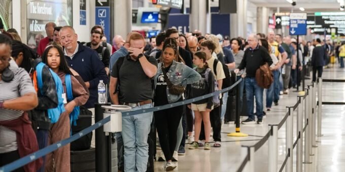 TSA agents working at an airport security checkpoint with travelers in the background.