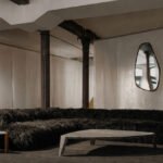 Interior view of ATRA FORM's New York gallery, showcasing minimalist furniture and a dark, textured carpet, with a Pyramid Chair and Chronos Light Sculpture visible.