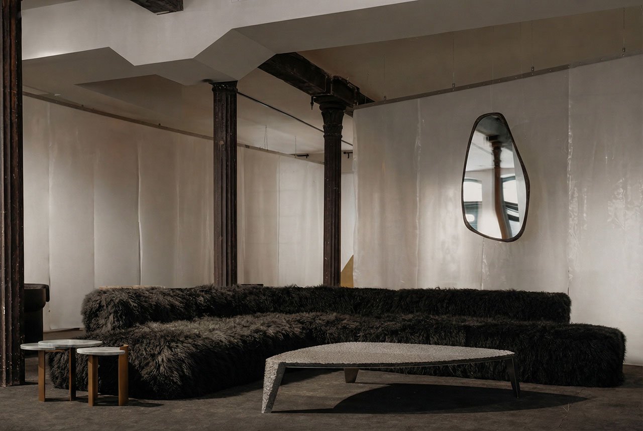 Interior view of ATRA FORM's New York gallery, showcasing minimalist furniture and a dark, textured carpet, with a Pyramid Chair and Chronos Light Sculpture visible.