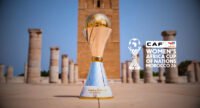 Vue aérienne d'un stade de football moderne au Maroc, symbolisant l'accueil de la CAN féminine 2026, avec un ciel bleu estival.
