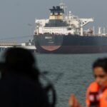 Oil tankers navigating the Strait of Hormuz with a backdrop of rising Brent crude oil prices on a digital display.