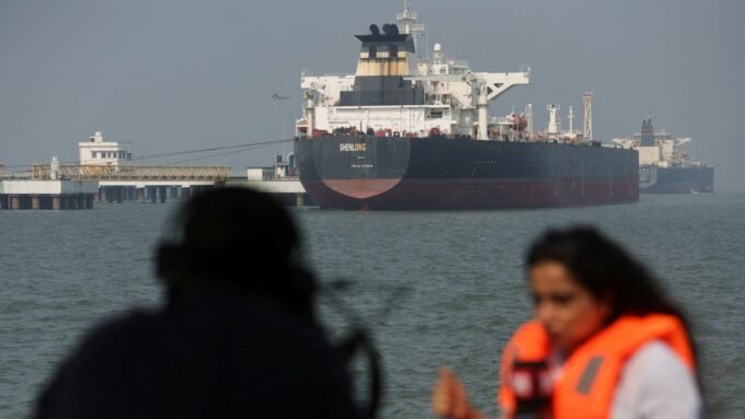 Oil tankers navigating the Strait of Hormuz with a backdrop of rising Brent crude oil prices on a digital display.