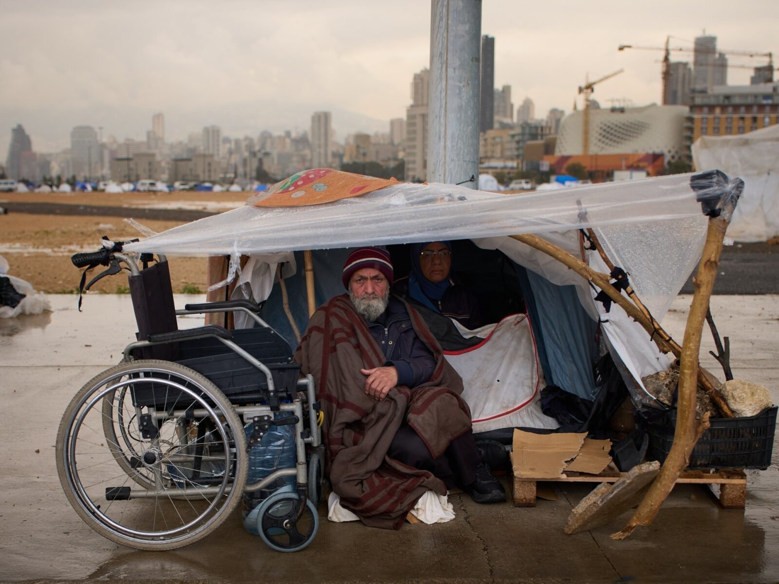 صورة تظهر عائلات نازحة من جنوب لبنان تبحث عن مأوى مؤقت في ظل الظروف الجوية القاسية، مما يعكس الأزمة الإنسانية المتفاقمة.
