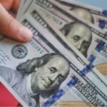 صورة تظهر عملة الدولار الأمريكي مع رسوم بيانية اقتصادية صاعدة، تعكس ارتفاع قيمته في الأسواق العالمية.