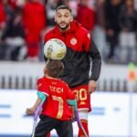 صورة النجم حكيم زياش وهو يصافح الطفل يونس بابتسامة في ملعب دونور، في لقطة تعبر عن التضامن والإنسانية.