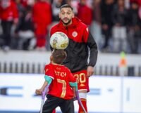 صورة النجم حكيم زياش وهو يصافح الطفل يونس بابتسامة في ملعب دونور، في لقطة تعبر عن التضامن والإنسانية.