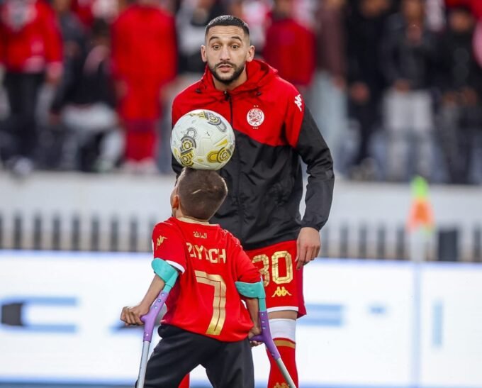 صورة النجم حكيم زياش وهو يصافح الطفل يونس بابتسامة في ملعب دونور، في لقطة تعبر عن التضامن والإنسانية.