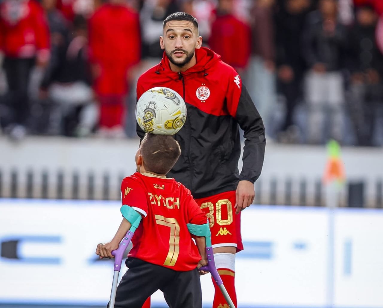 صورة النجم حكيم زياش وهو يصافح الطفل يونس بابتسامة في ملعب دونور، في لقطة تعبر عن التضامن والإنسانية.