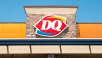 A classic Dairy Queen vanilla soft-serve cone with the iconic curl, held against a bright background.