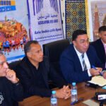 Vue aérienne de la médina de Fès avec des coureurs traversant ses rues étroites, longeant les remparts et s'approchant de la porte emblématique de Bab Boujloud, lors de la course 'De Bab en Bab'.