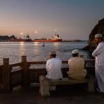 Des vraquiers et des pétroliers sont amarrés dans le golfe d’Oman, face au port de Sohar, tandis qu’une famille se retrouve pour prendre le thé près de la plage, à Shinas (Oman), le 27 mars 2026.