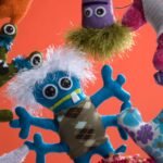 A whimsical collection of colorful, hand-sewn plush monsters, each uniquely designed with different shapes, eyes, and features, embodying the "free-range" crafting spirit.