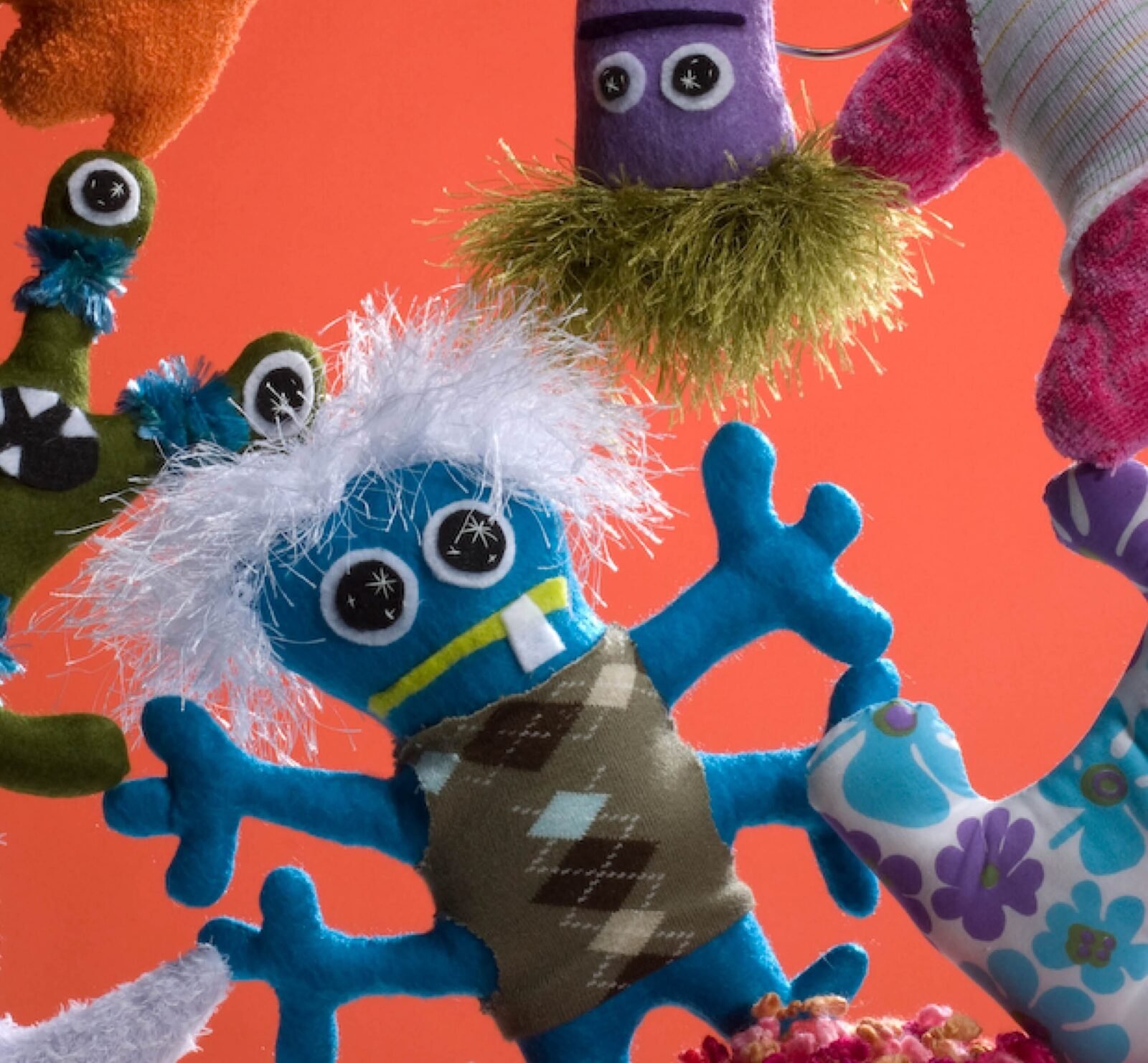 A whimsical collection of colorful, hand-sewn plush monsters, each uniquely designed with different shapes, eyes, and features, embodying the "free-range" crafting spirit.