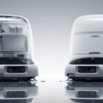 A DJI Romo robot vacuum, a sleek white disc-shaped device, on a wooden floor.