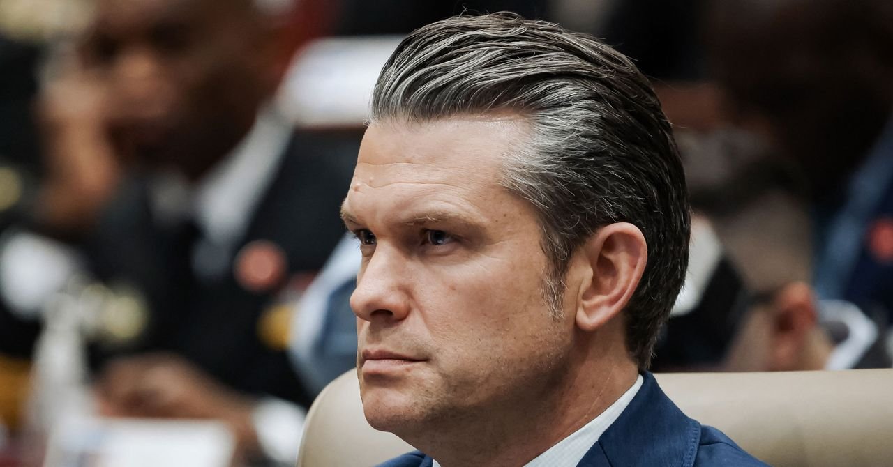 Secretary of Defense Pete Hegseth speaking at a press conference, with a blurred image of the US-Mexico border in the background.