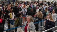 Travelers queueing in a long security line at a busy airport checkpoint, highlighting the impact of staffing shortages.