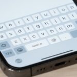 An iPhone screen displaying a keyboard with text being typed, symbolizing the upcoming iOS 26.4 keyboard fix.