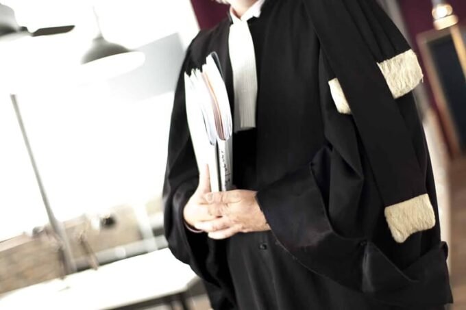 Une balance de justice stylisée, symbolisant l'équilibre et la profession d'avocat, avec un arrière-plan flou de documents juridiques et de mains en discussion, évoquant les tensions et les négociations autour du projet de loi.