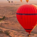 Des montgolfières colorées s'envolant au-dessus des paysages ocres de Marrakech, avec les montagnes de l'Atlas en arrière-plan, symbolisant le boom touristique et le besoin de régulation.