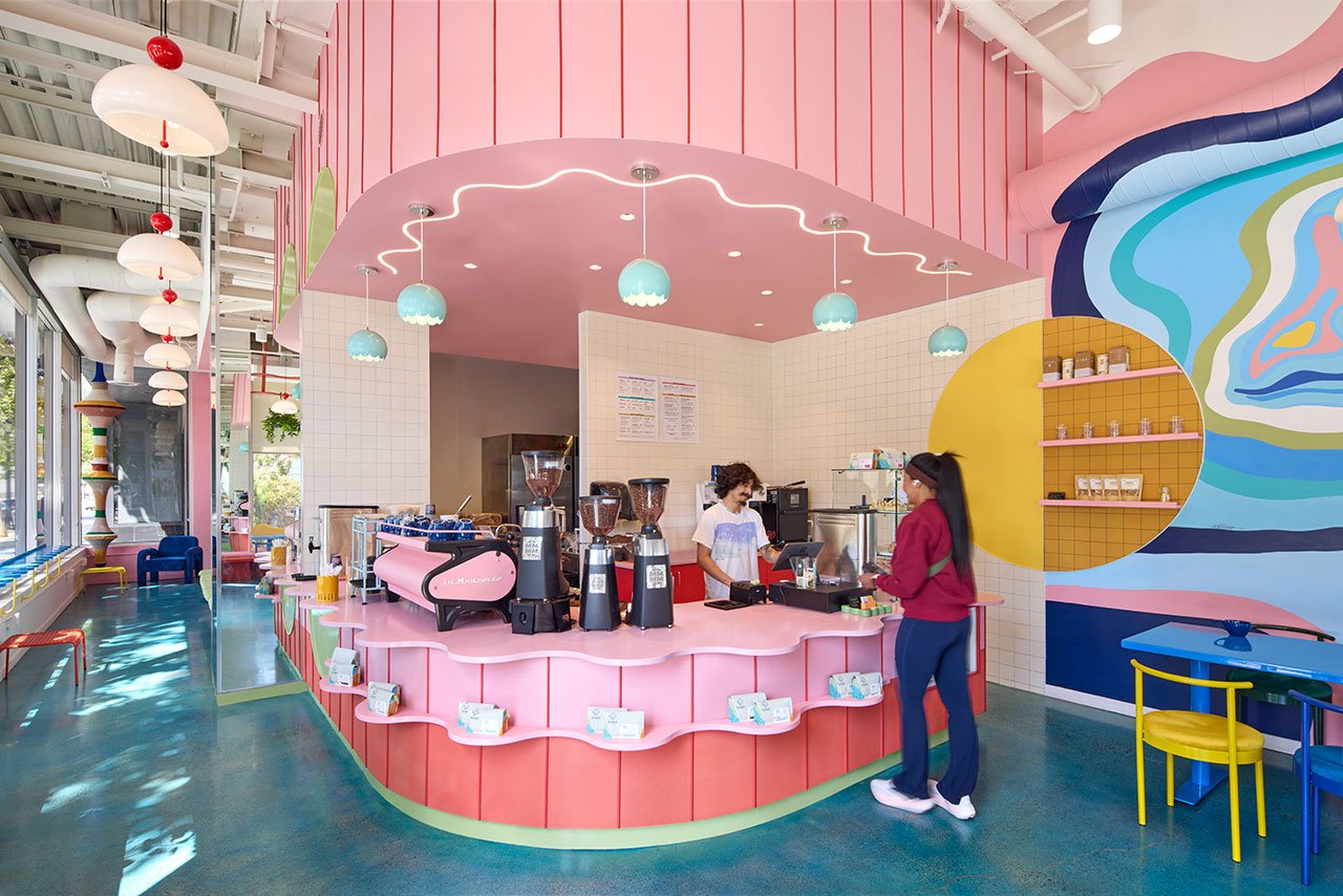 Interior view of Voyager Craft Coffee's maximalist micro-café designed by Studio BANAA, featuring a pink perforated metal coffee bar, colorful murals, and playful design elements.